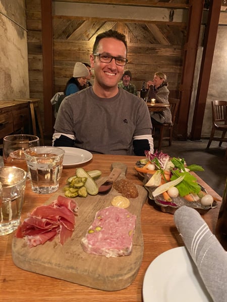 Tom, a white brunette male in gray sweater, at table with charcuterie board and crudités platter at The Bull and Beggar in Asheville, NC
