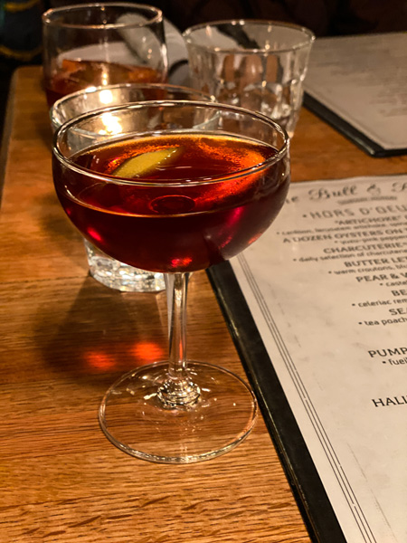 The Bull and Beggar Restaurant Asheville BC with dark orange and brown cocktail next to menu on table