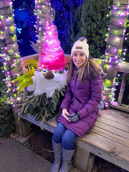 Bush decorated like a gnome with red hat with lights and beard next to Christine, a white brunette woman in a purple jacket with jeans and boots at Winter Lights in Asheville, NC