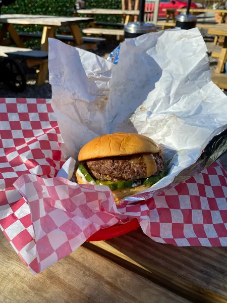 Baby Bull Burgers Asheville NC River Arts District with double burger patty on bun in basket with red checkered paper on picnic table outside