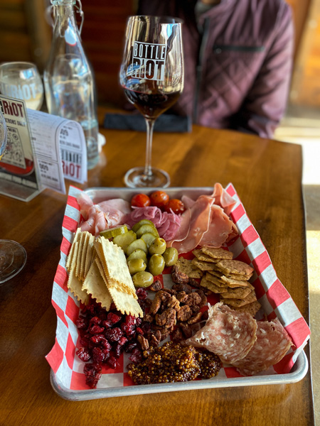 Bottle Riot Charcuterie Asheville NC with meats, crackers, jam, and olives on silver tray with paper