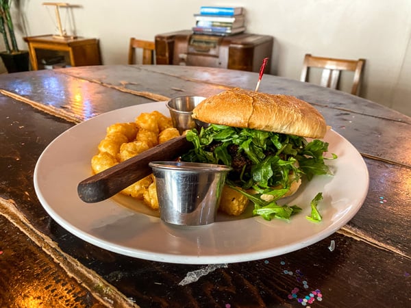 Rankin Vault Cocktail Lounge Burger in Downtown Asheville NC with beef hamburger with lettuce, bun, and tater tots on white plate and table with steak knife