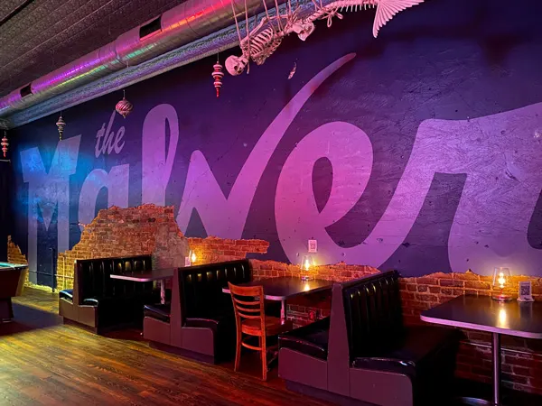 The Malvern Bar in West Asheville NC with mural with name, booths, and purple lighting