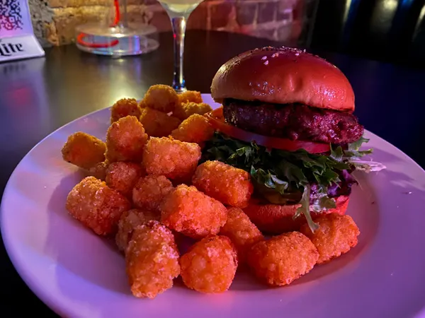 The Malvern burgers in West Asheville NC with burger with lettuce, tomato, and bun with tater tots and mood lighting