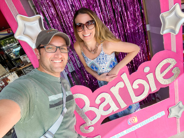 Christine and Tom, white brunette male and female, taking a selfie in a pink, life-size Barbie box at the Grail Moviehouse in Asheville, NC