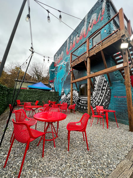 Guajiro Restaurant in the River Arts District in Asheville, NC with bright red tables and chairs and mural on side of Asheville Cotton Mill Studios that has an image of a dog and the words "que Linda"