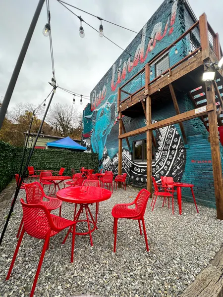 Guajiro Restaurant in the River Arts District in Asheville, NC with bright red tables and chairs and mural on side of Asheville Cotton Mill Studios that has an image of a dog and the words "que Linda"