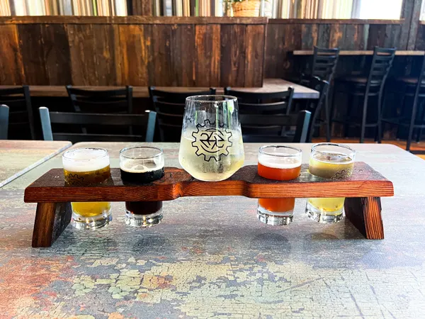 River Arts District Brewing Company Asheville NC with flight of yellow, brown, and orange beers on table with yellow cider in a separate glass and beer steel fermentation tanks in the background