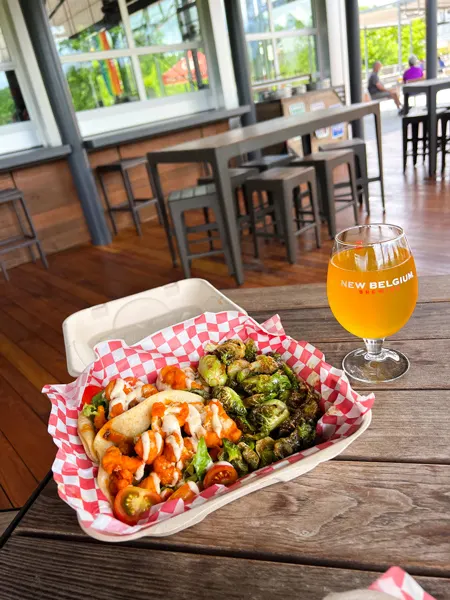 The Smokin Onion Food Truck at New Belgium Brewing Company in Asheville with fried Brussel sprouts and Buffalo cauliflower vegan tacos in takeaway container with orange hard seltzer