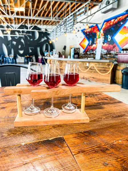 pleb urban winery in Asheville River Arts District with Flight of three red wines on brown table and bar with two murals in the background