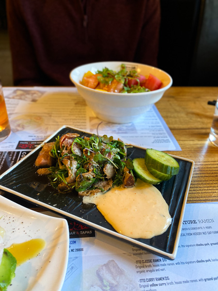 Beef Yakitori Itto Ramen Bar Restaurant Asheville with beef, sauces, and cucumber on plate with poke bowl in background