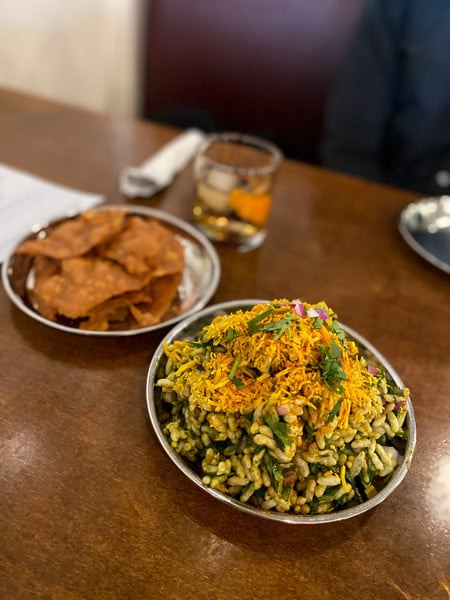 Bhel puri Chai Pani Indian Street food Asheville NC with two silver bowls filled with puffed rice and cucumber and fried flour chips