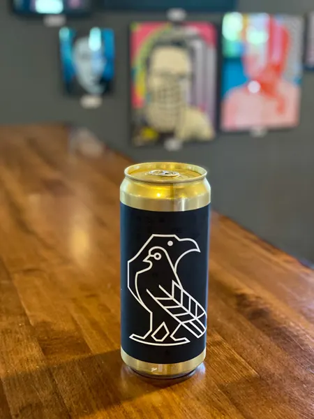 Eurisko Beer Company Asheville NC with can of beer with two birds on it on brown table with blurred paintings in background
