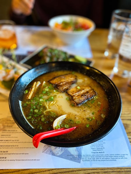 Bowl of ramen soup with pork and red spoon on table at Itto Ramen Bar and Tapas in Asheville, NC (West Asheville location) 