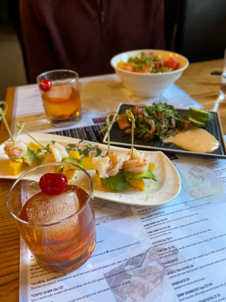 Itto Ramen Bar and Tapas Asian Restaurant Asheville NC with two Old Fashioned cocktails with cherry on table, shrimp and mango skewers, and poke bowl in background
