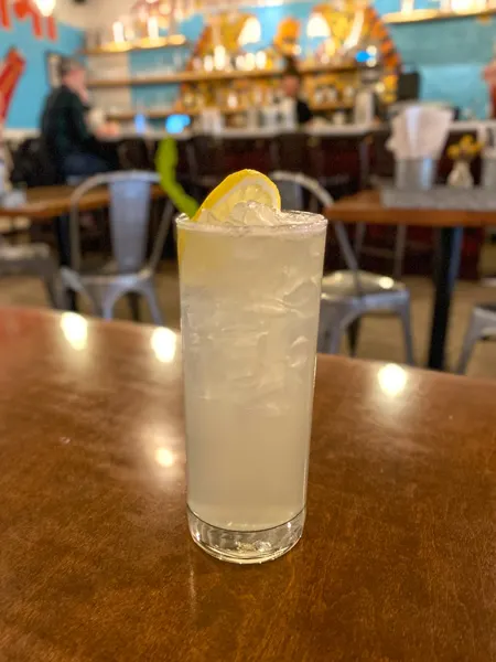 Lavender Lemonade at Chai Pani Restaurant in Asheville NC with light white cocktail on brown table with lemon garnish in tall glass