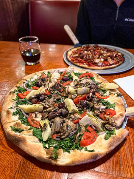 828 Family Pizzeria Pizza in Asheville NC with regular crust on pizza plate, no cheese, and topped with mushrooms, artichokes, tomatoes, kalamata olives and spinach