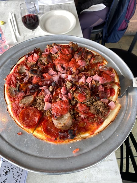 Apollo Flame Bistro gluten free pizza in Asheville with meats, pepperoni, and sausage on silver tray with glass of red wine