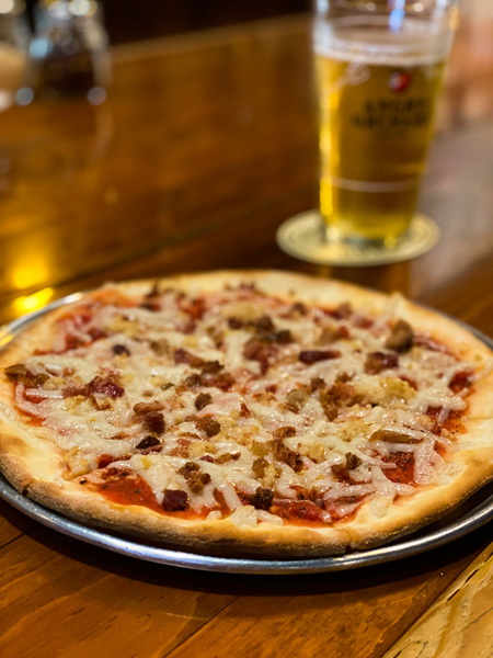 Barleys Taproom Downtown Asheville Pizza with vegan cheese, meat, and gluten-free pizza crust on bar with class of yellow colored beer