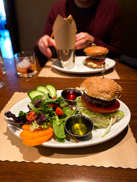 Bone And Broth North Asheville Burger with two white plates with burgers, one with a side salad and the other with fries