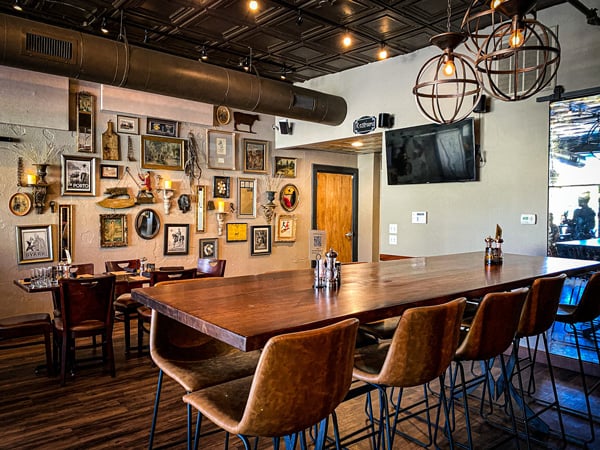 Bone and Broth Restaurant Asheville NC with brown tables and chairs with wall filled with mismatched pictures and picture frames and sphere shaped lights