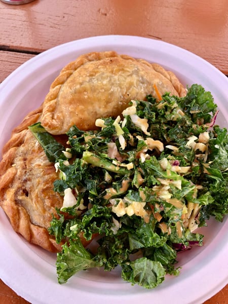 Cecilia's Kitchen food truck and restaurant Asheville with 2 brown empanadas next to kale salad on white paper plate