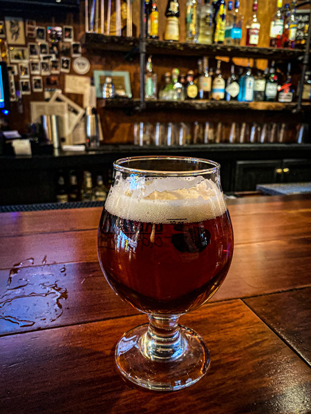 Foggy Mountain Brew Pub Asheville NC with local amber colored craft beer at bar with bottles and taps blurred in background