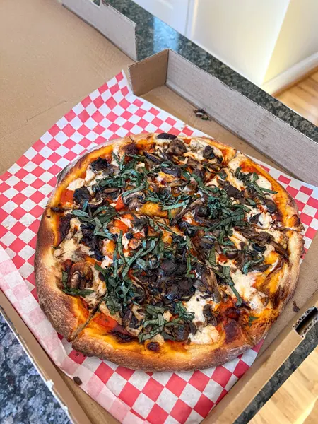 Laughing Seed in Asheville NC pizza topped with basil, vegan cheese, sun dried tomatoes, garlic, and sauce in takeout box on red checkered paper