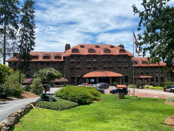 Omni Grove Park Inn luxury resort North Asheville with front of the hotel with brown stone and orange roof and circle of green grass with valet parking out front and blue sky with clouds