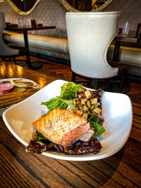 Salmon at Red Stag Grill in Asheville NC with white plate filled with pink salmon over green lettuce with apples and curried walnuts