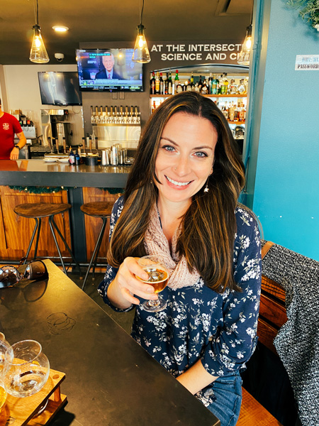 White Labs Brewing Kitchen And Tap Asheville NC with white brunette woman sitting at table in front of flight of beer with one beer flight glass in her hand and bar in the background