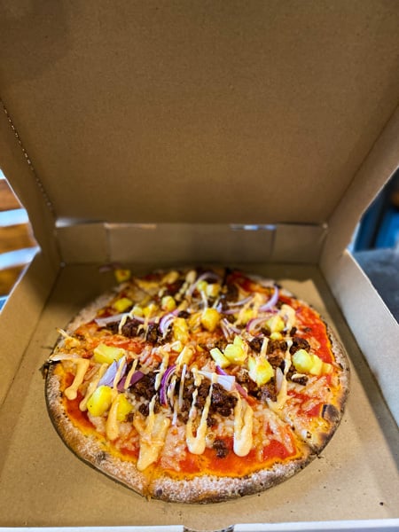 White Labs Brewing Kitchen And Tap Downtown Asheville pizza place with pizza in delivery box with gluten-free crust, vegan cheese, pineapple, meats, and a sauce
