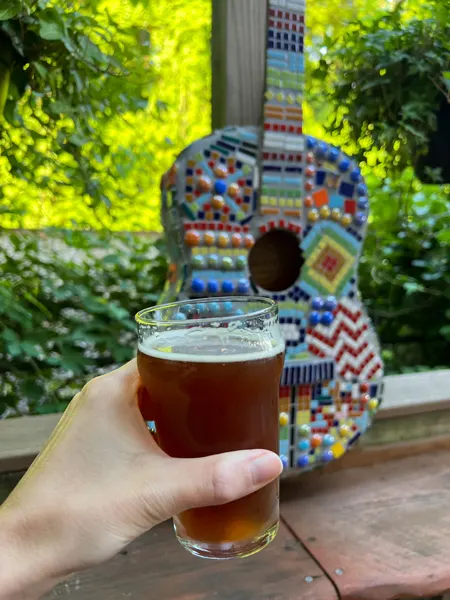 Asheville Guitar Bar in Asheville, NC with white hand holding up half pour of brown beer in front of guitar decor on outside back patio