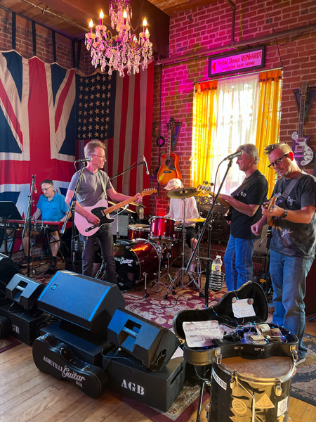 Asheville Guitar Bar in River Arts District with band playing guitars and singing in front with British and American flags on side