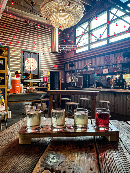 Bens Tune Up Sake Bar Asheville with sake flight ranging from yellows to red on table with bar in background