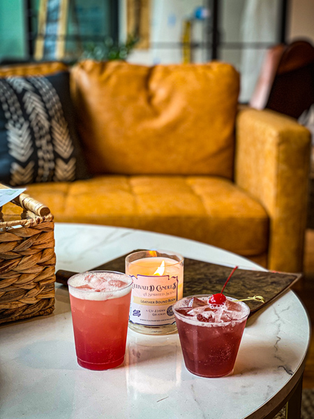 Cultivated Cocktails Downtown Asheville NC tasting room with yellow-brown couch, two redish cocktails, and a lit candle on table