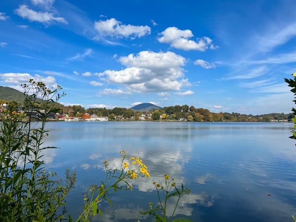 Lake Junaluska NC October with blue water, bright but cloudy sky, yellow flowers, and trees changing colors