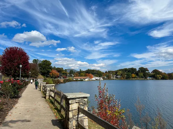 Lake Junaluska Rose Wall Fall Foliage NC with paved walking perimeter trail, red and orange trees, blue cloudy sky and blue water lake
