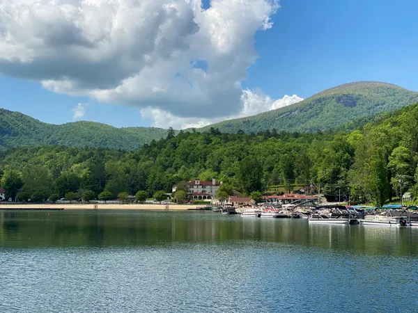 Lake Lure Beach North Carolina with lake, sandy shore, boats and buildings surrounded by Chimney Rock with blue sky and clouds