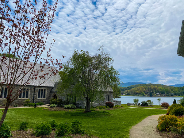 Memorial Chapel Columbarium Lake Junaluska with church and walking path with green trees with lake behind them and blue cloudy sky