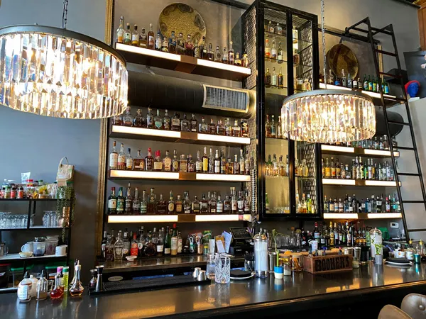 The Times Bar Asheville NC with two chandeliers, brown bar top, and rows of liquor on black shelving