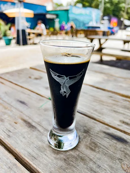 The Whale Bar in Asheville, NC with image of flight glass with whale logo filled with dark brown beer on picnic table outside