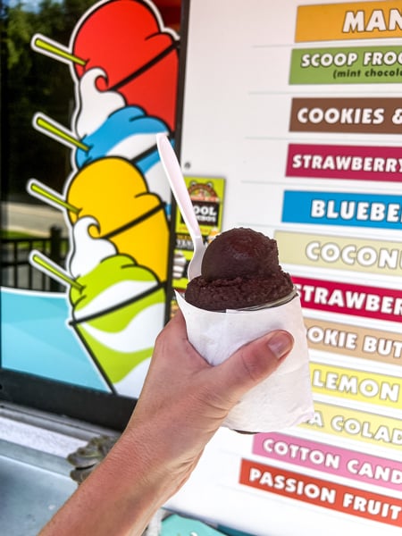 Jeremiah's Italian Ice Asheville NC with white hand holding up black raspberry Italian ice in front of colorful menu and order window