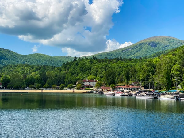 Lake Lure Washburn Marina NC with dark blue green lake and shore with buildings and boats and mountains behind them