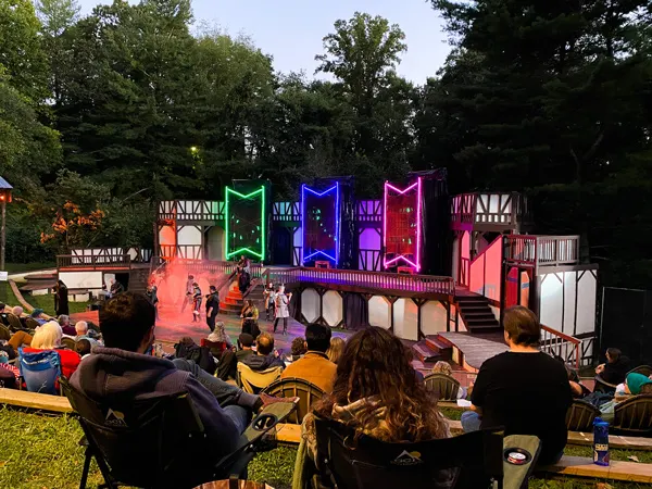 Montford Park Players Shakespeare Asheville with Shakespeare stage, couple sitting in front with law chairs, and blue, green, and red lights in shape of banners on stage