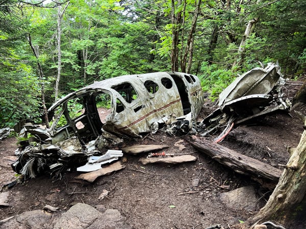 Cessna Plane Crash Site Maggie Valley NC with crashed white Cessna plane with no windows and broken wings next to smashed engine in woods