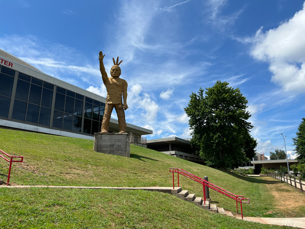 Clyde A. Erwin High School with green lawn, steps going up to school complexes like theater and gym and large statue of Indigenous community member