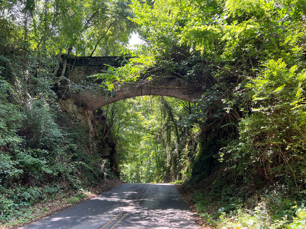 Helens Bridge Asheville NC with image of older but well-kept up stone bridge over two lane road with green trees