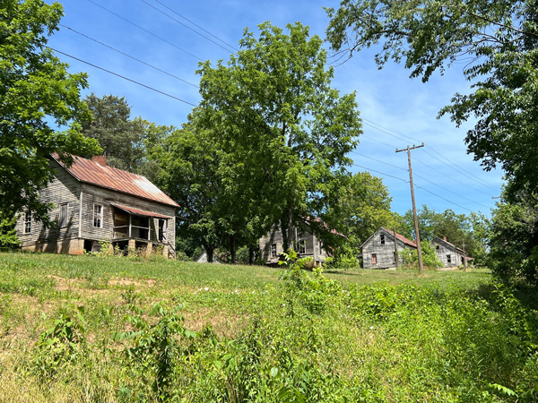 Henry River Mill Village NC Abandoned Places with three dilapidated wooden house structures with green grass, power lines and sky