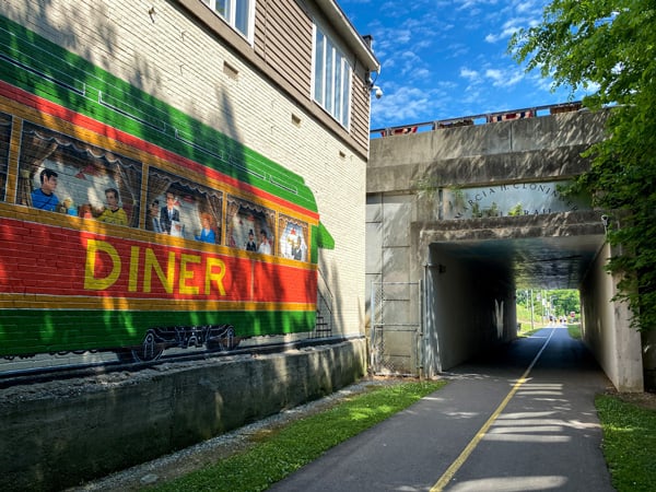 Marcia H Cloninger Rail-Trail Lincolnton NC with mural of train car and two lane walking and biking paved trail that goes under a walking bridge